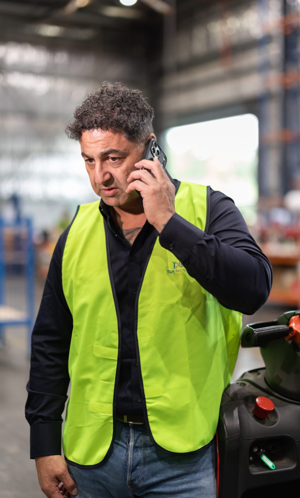 James Marroun from TLH Group communicates on the phone while wearing a safety vest in a warehouse environment.